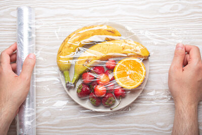 Manos Masculinas Envolviendo un plato de frutas con film alimenticio