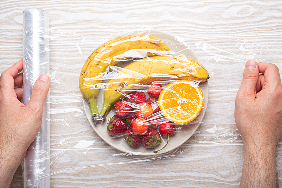 Manos Masculinas Envolviendo un plato de frutas con film alimenticio